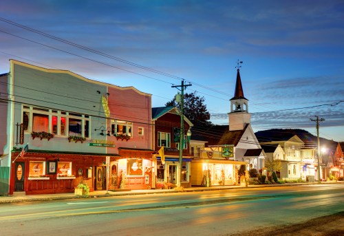Charming small-town street at dusk, featuring colorful buildings and a church steeple against a twilight sky.