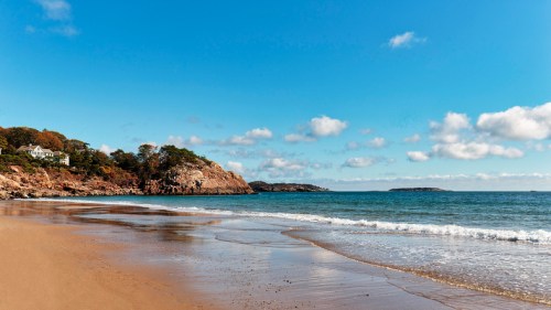 A serene beach scene with golden sand, gentle waves, and a clear blue sky dotted with fluffy clouds.