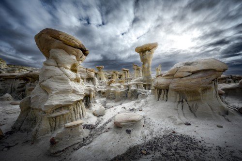 Bizarre rock formations rise from a sandy landscape under a dramatic, cloudy sky.