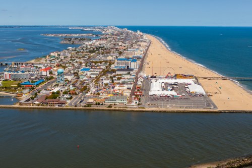 Aerial view of a coastal city with sandy beaches, amusement park, and waterfront along a blue ocean.