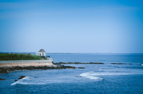 A serene coastal view featuring a small gazebo by the water, with gentle waves and a clear blue sky.