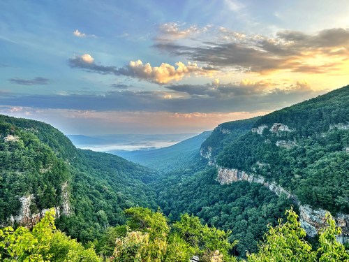 A scenic view of a lush green valley surrounded by mountains under a colorful sky at sunset.