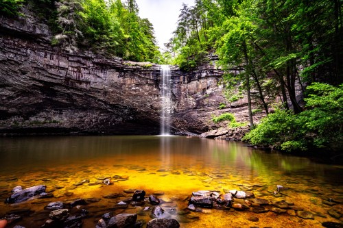 A serene waterfall cascades into a clear pool, surrounded by lush greenery and rocky cliffs.