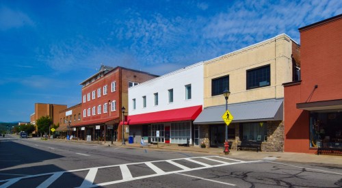 A quiet street scene featuring a row of storefronts with varied architectural styles under a blue sky.