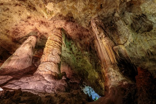 Stalactites and stalagmites in a colorful cave, showcasing unique rock formations and illuminated textures.