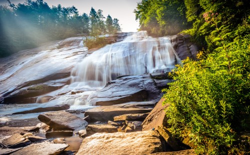 A serene waterfall cascades over smooth rocks, surrounded by lush greenery and soft morning light.