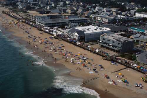 Aerial view of a beach with people, umbrellas, and nearby buildings along the shoreline.