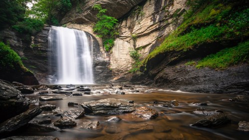 A serene waterfall cascades over rocky cliffs, surrounded by lush greenery and a tranquil riverbed.