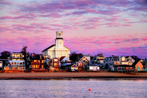 A coastal scene at sunset featuring colorful houses and a church against a vibrant sky.
