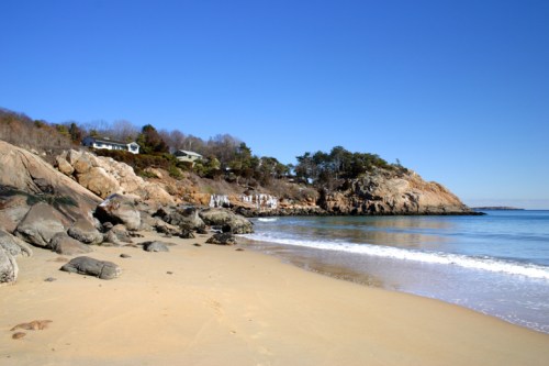 A serene beach scene with golden sand, rocky shorelines, and clear blue water under a bright blue sky.