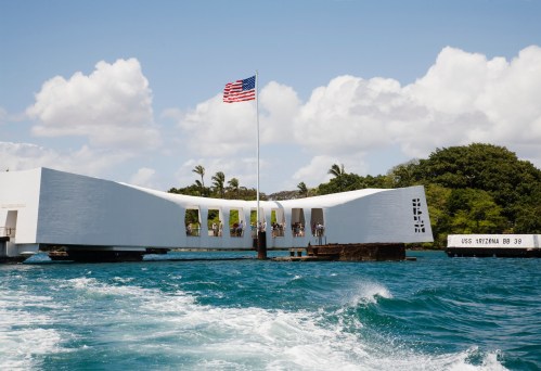 The USS Arizona Memorial in Pearl Harbor, with an American flag and clear blue water in the foreground.