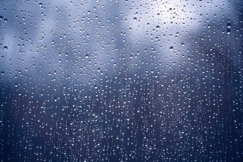 Close-up of raindrops on a window, creating a blurred, moody background with soft gray tones.