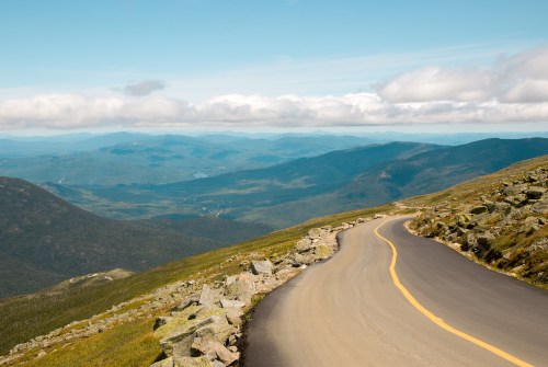 A winding road curves through a mountainous landscape under a blue sky with fluffy clouds.