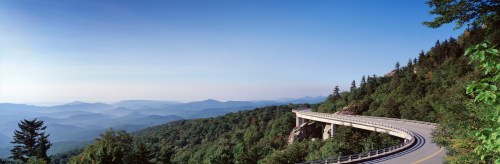 A scenic view of a winding road through lush green mountains under a clear blue sky.