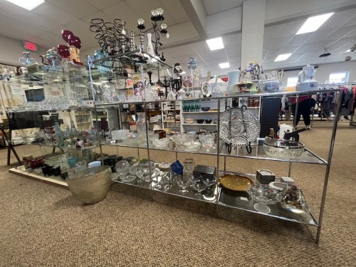 A display shelf filled with various glassware, decorative items, and kitchenware in a store setting.