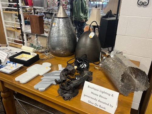 A display of unique metal decor items and lighting on a wooden table, with a sign about donations from Gleo On Bank.