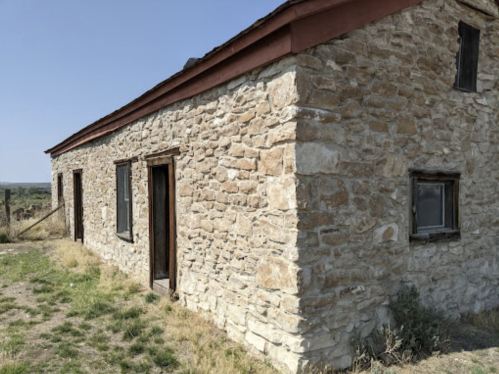 A weathered stone building with a red roof, surrounded by grass and a clear blue sky.