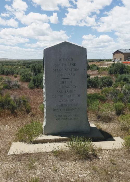 A stone monument commemorating the Old South Bend Stage Station, built in 1859, surrounded by sparse vegetation.