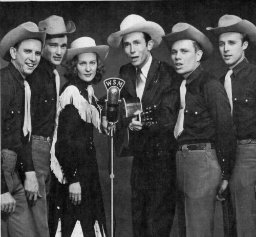 A vintage black-and-white photo of six musicians in cowboy attire, gathered around a microphone labeled "WSM."
