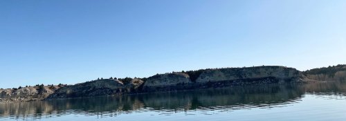 A serene lake reflecting a rocky shoreline under a clear blue sky.