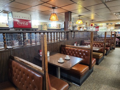 Cozy diner interior with brown leather booths, wooden dividers, and vintage Coca-Cola signage. Warm lighting creates a welcoming vibe.