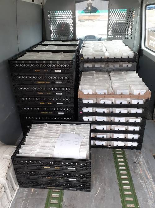 Interior of a delivery van filled with stacked crates containing sealed packages.