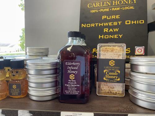 A display of Carlin Honey products, including elderberry infused honey and comb honey, with metal containers in the background.