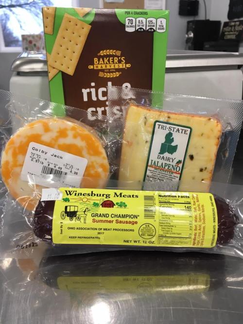 A selection of cheese, crackers, and summer sausage packaged together on a countertop.