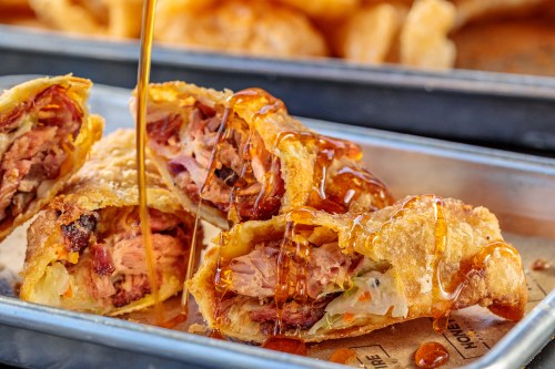 Crispy fried rolls filled with meat and vegetables, drizzled with a sweet sauce on a metal tray.