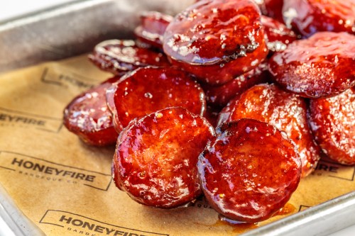 Close-up of glossy, sliced barbecue sausage on parchment paper, showcasing a rich, caramelized glaze.