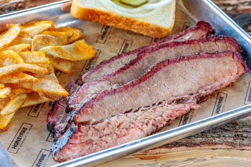 A tray with sliced brisket, crispy potato chips, and a slice of bread with onions on top.