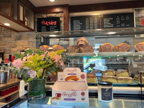 A café display with pastries, a flower arrangement, and a menu board in the background.