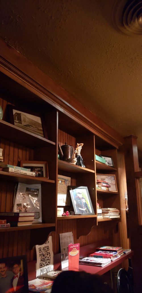 A wooden shelf filled with books, photos, and decorative items in a cozy restaurant setting.