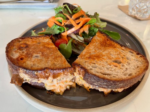 A toasted sandwich with melted filling, served with a side salad of mixed greens and shredded carrots.