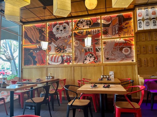A vibrant restaurant interior featuring a colorful mural, wooden accents, and red chairs at wooden tables.