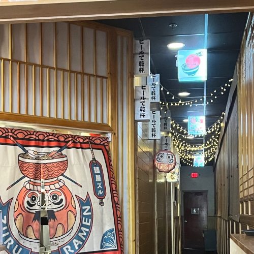 A cozy ramen restaurant hallway with decorative lanterns, banners, and string lights creating a warm atmosphere.