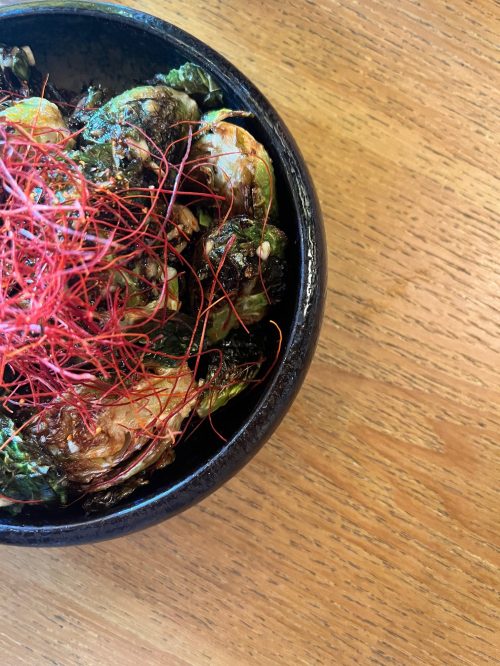 A black bowl filled with crispy shrimp topped with red threads, placed on a wooden surface.