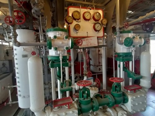 Industrial machinery with valves, gauges, and pipes, featuring red and green components in a well-lit environment.