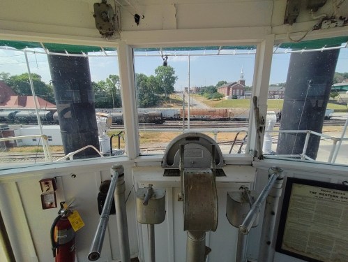 View from the pilot house of a riverboat, showing a landscape with train tracks and buildings in the background.