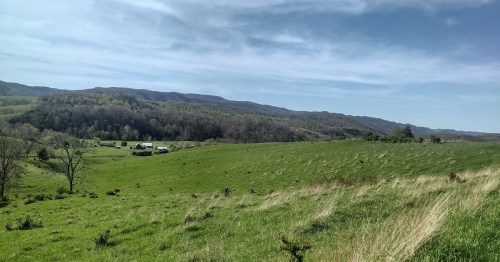 A scenic landscape featuring rolling green hills, distant mountains, and a clear blue sky.