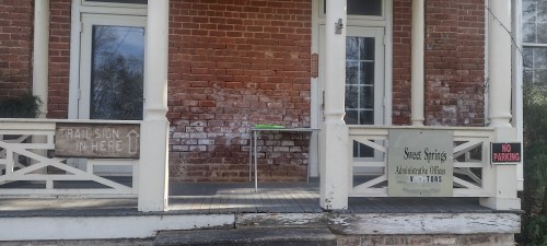 A porch with brick walls, a table, and signs for trail directions, street springs, and no parking.