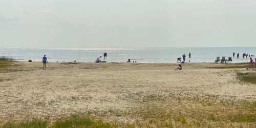A sandy beach with people walking and relaxing by the water under a hazy sky.