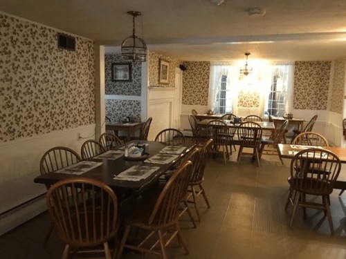 Cozy dining area with wooden tables and chairs, floral wallpaper, and large windows letting in natural light.