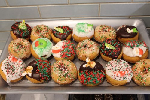 A tray of festive donuts decorated with icing, sprinkles, and holiday-themed toppings in red and green.