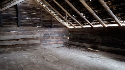 An empty, rustic wooden attic with exposed beams and a dusty floor, illuminated by soft light.