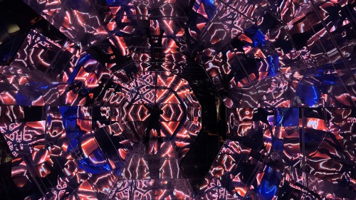 A mirrored tunnel with vibrant red and blue lights creating a kaleidoscopic effect.