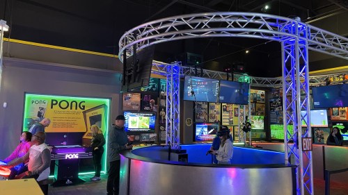A vibrant arcade with colorful lights, gaming stations, and multiple screens displaying games and information.