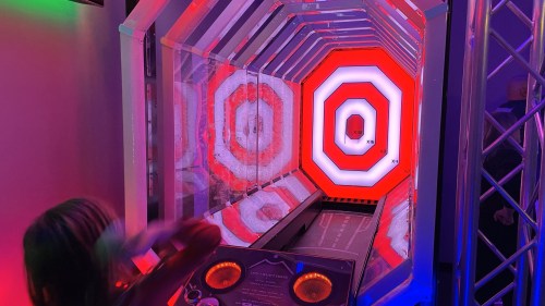 A colorful arcade game with illuminated targets and a player preparing to throw a ball.