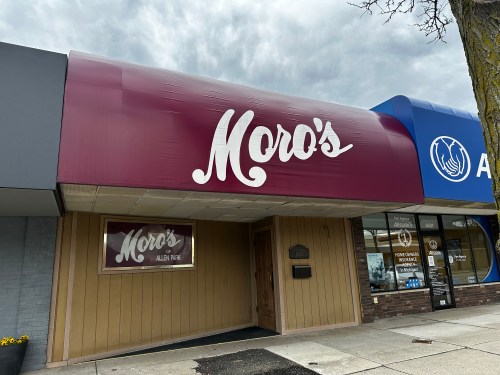 Exterior of Moro's restaurant with a maroon awning and wooden paneling, located in a commercial area.