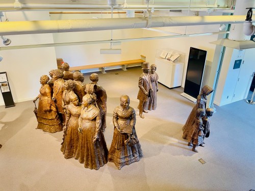 A group of bronze sculptures depicting women in historical dresses, arranged in a gallery space.